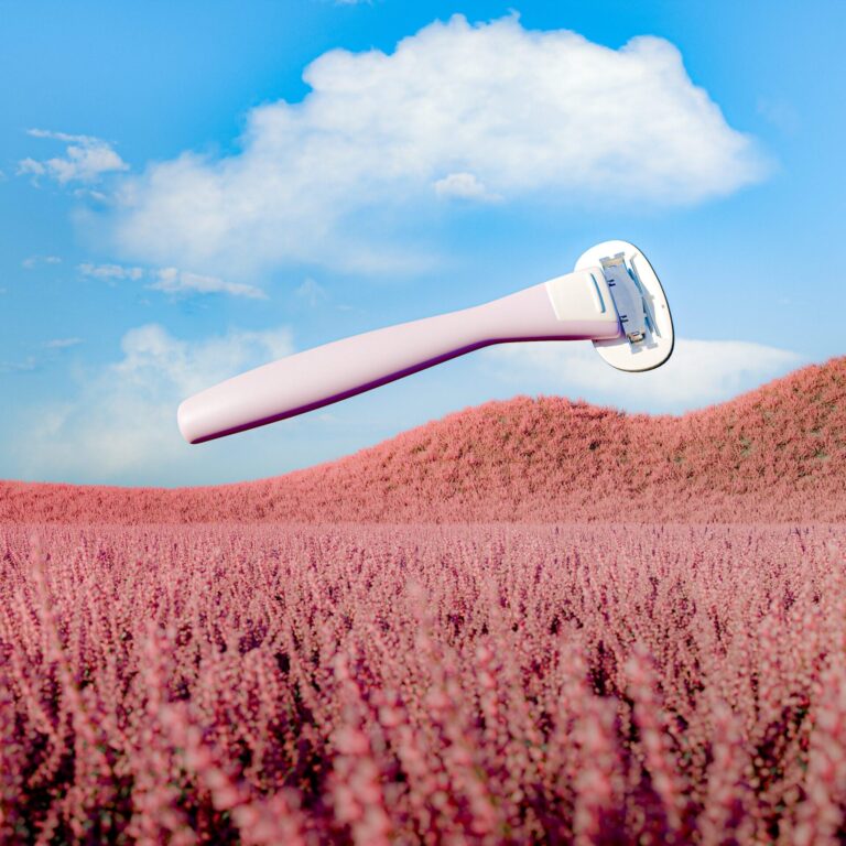 Vaaleanpunainen shaver leijuu ilmassa kukkaniityn yläpuolella. Taustalla näkyy sininen taivas ja valkoisia pilviä.