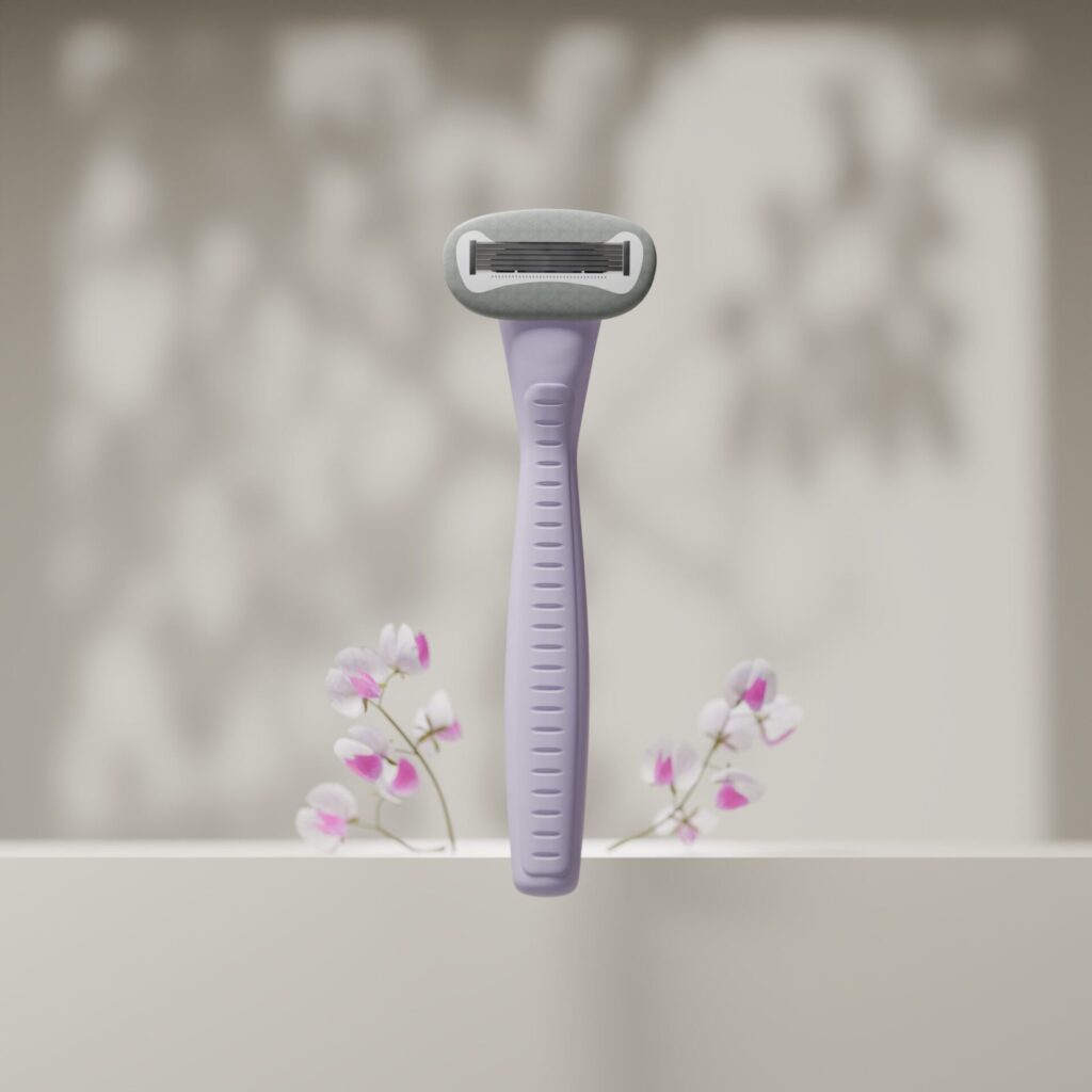 Vaaleanvioletti sheiveri seisoo pystyasennossa vaaleaa taustaa vasten, taustalla näkyy pehmeitä varjoja ja hennon vaaleanpunaisia kukkia.